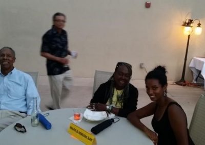 photo of 3 people at table while one person walks past