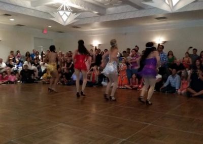 four women stand on dance floor while observers watch