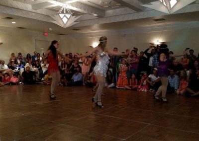 four women stand on dance floor while observers watch