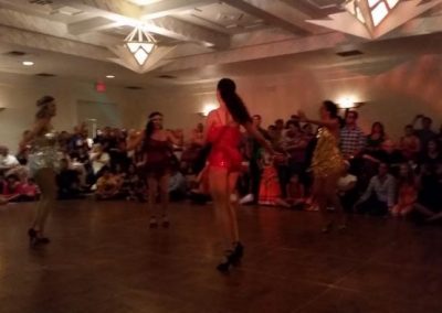 four women stand on dance floor while observers watch